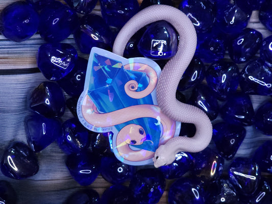 Holographic sticker with a snake design on blue tumbled rocks.
